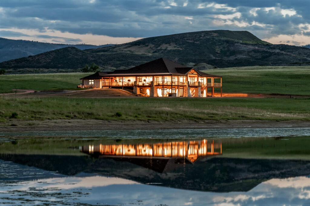 A Colorado mansion overlooking a small lake in the evening, backdropped by the Front Range