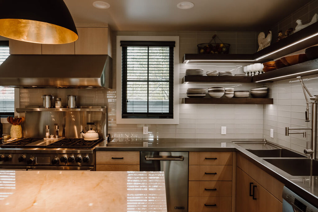 A modern restaurant-style home kitchen crafted in steel and stone. Floating shelves with undercabinet lighting and modern fixtures.
